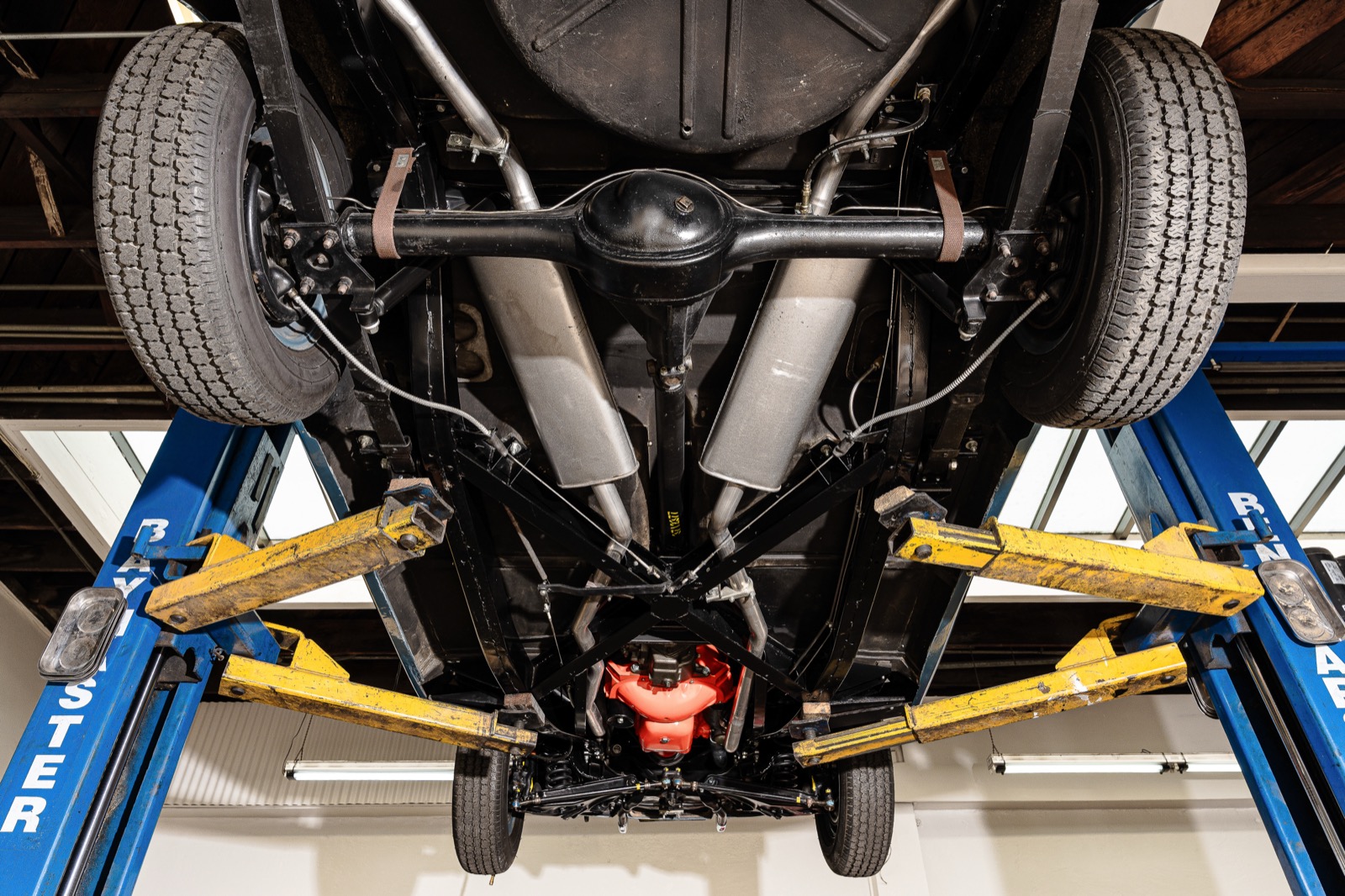 Full underside of a classic car raised on a two-post lift, showing the rear axle, dual exhaust, and frame