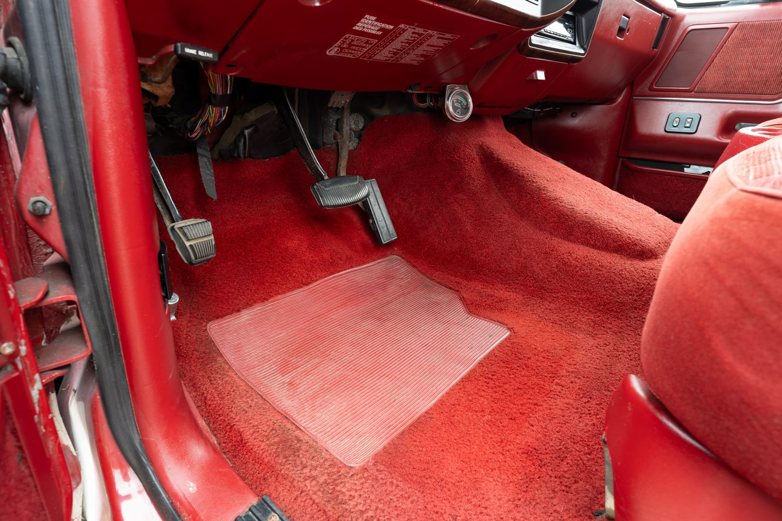 The same 1989 Ford Bronco footwell, framed identically, with the mat removed to show the red carpet beneath