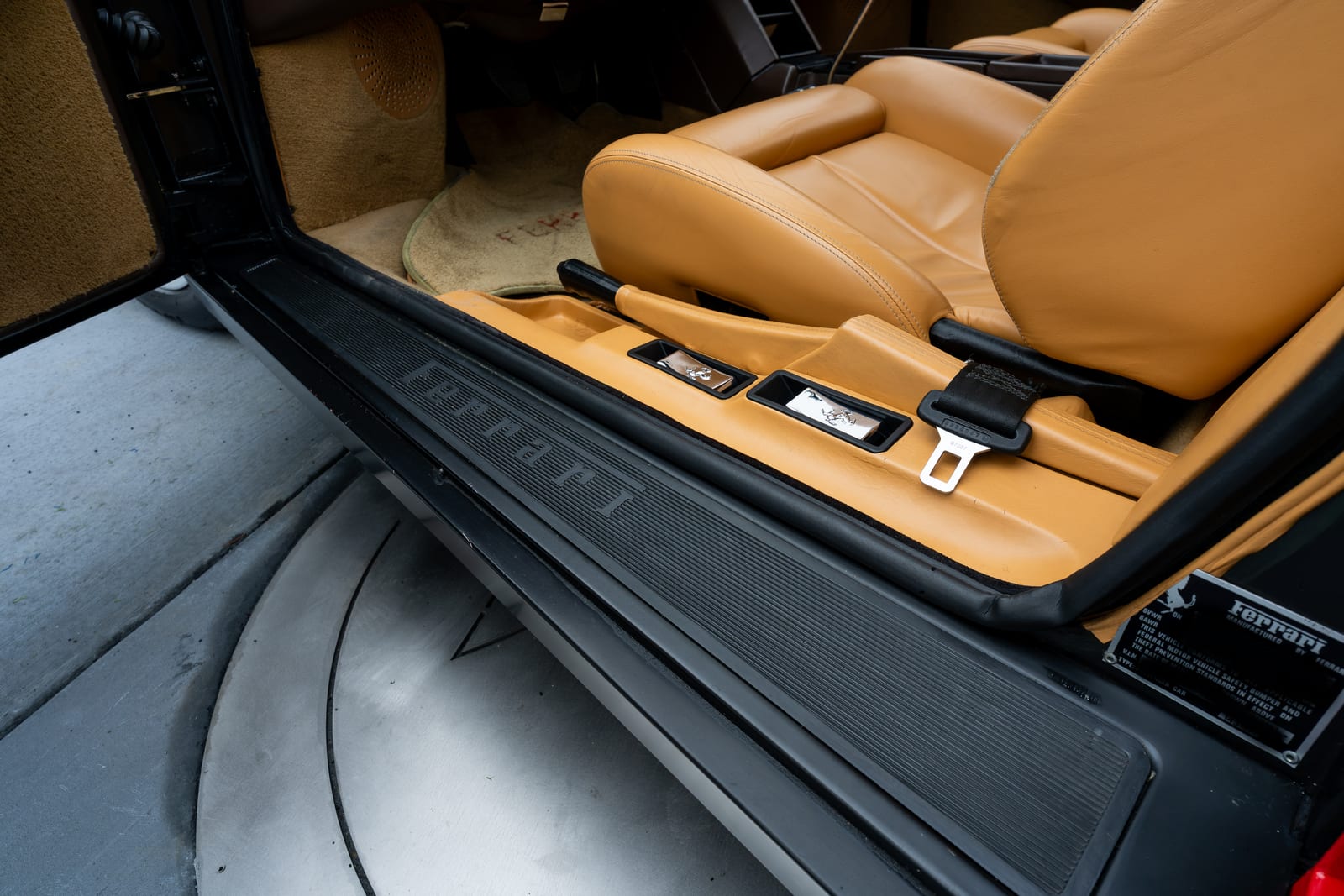 Ferrari lettering molded into the black door sill of a 1990 Testarossa, tan leather seats inside the open door
