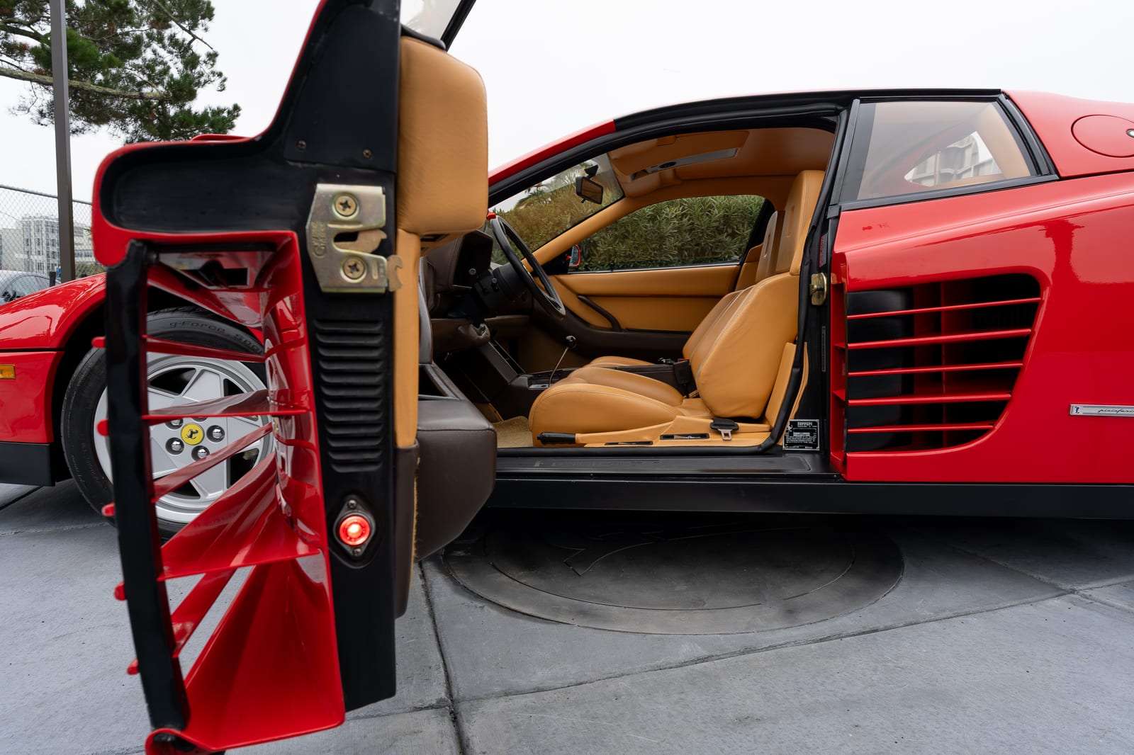 Open driver door of a red 1990 Ferrari Testarossa, the side strakes continuing across the inside edge of the door