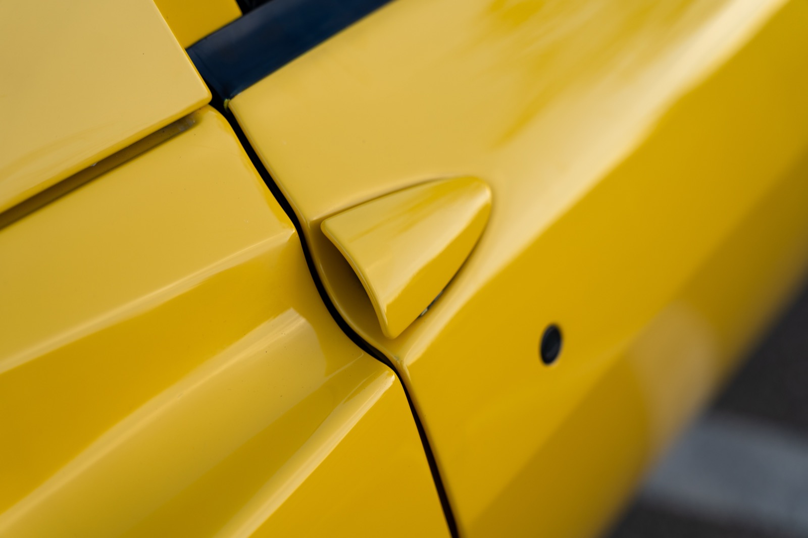 Yellow scooped door handle of a 2004 Ferrari 360 Spider photographed at an oblique angle across the door gap