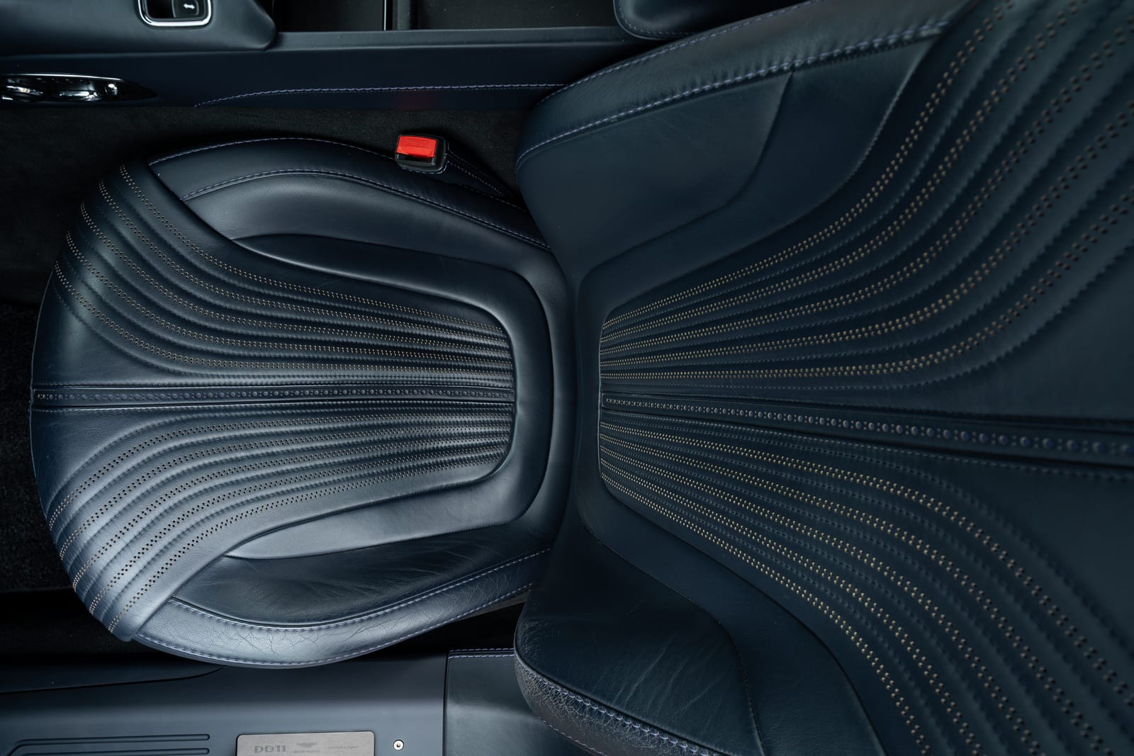 Top-down view of a 2017 Aston Martin DB11 driver seat in dark blue leather with perforated, stitched lines fanning across the cushion and backrest