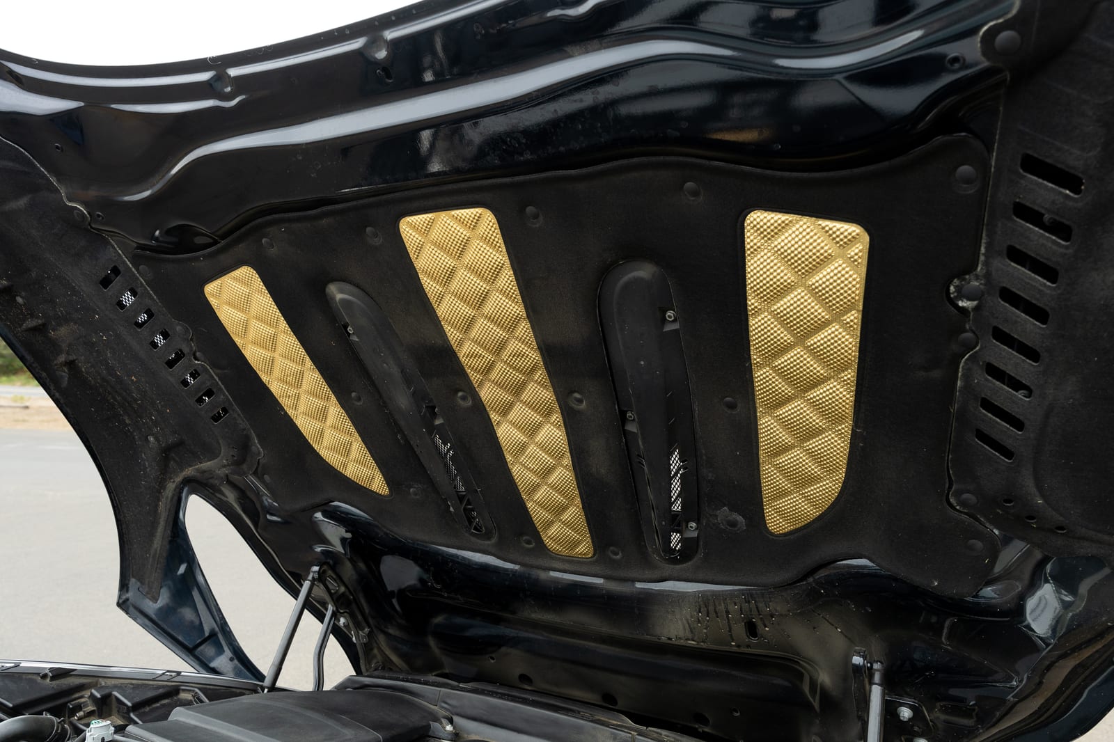 Gold quilted panels set into the black under-bonnet lining of a 2017 Aston Martin DB11 with the hood raised