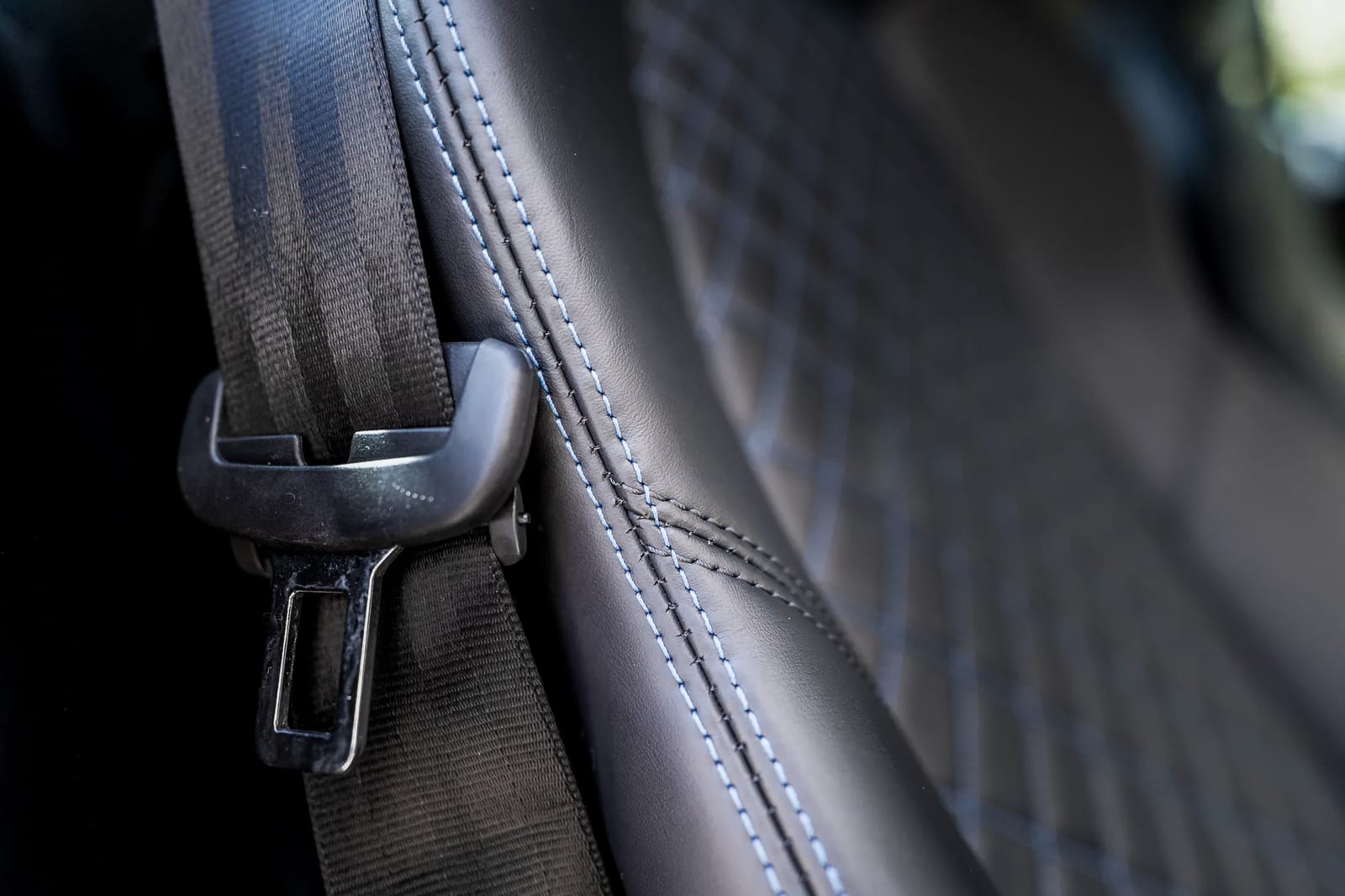 Close-up of blue contrast stitching along the seat edge of a 2017 Audi R8 V10 Plus, seat belt buckle in the foreground, diamond-quilted leather behind