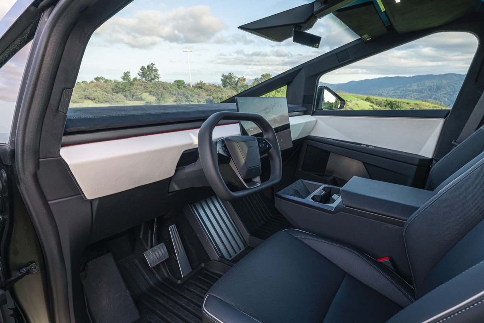 Driver's side interior of a Tesla Cybertruck Beast Foundation Series with green hills and sky visible through the windows